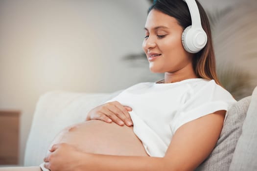 Woman, pregnant and relax while listening to calm music on sofa in healthy zen, wellness or meditation at home. Pregnant woman smile in relaxation holding tummy with headphones on living room couch.