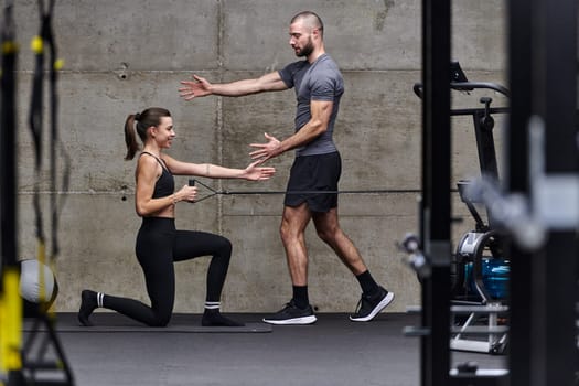 A muscular man assisting a fit woman in a modern gym as they engage in various body exercises and muscle stretches, showcasing their dedication to fitness and benefiting from teamwork and support.