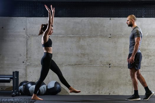 A muscular man assisting a fit woman in a modern gym as they engage in various body exercises and muscle stretches, showcasing their dedication to fitness and benefiting from teamwork and support.