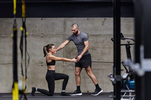 A muscular man assisting a fit woman in a modern gym as they engage in various body exercises and muscle stretches, showcasing their dedication to fitness and benefiting from teamwork and support.