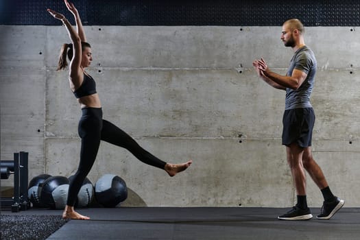 A muscular man assisting a fit woman in a modern gym as they engage in various body exercises and muscle stretches, showcasing their dedication to fitness and benefiting from teamwork and support.