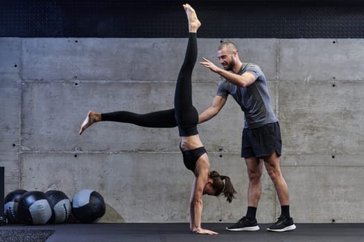 A muscular man assisting a fit woman in a modern gym as they engage in various body exercises and muscle stretches, showcasing their dedication to fitness and benefiting from teamwork and support.