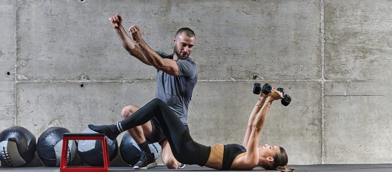 A muscular man assisting a fit woman in a modern gym as they engage in various body exercises and muscle stretches, showcasing their dedication to fitness and benefiting from teamwork and support.