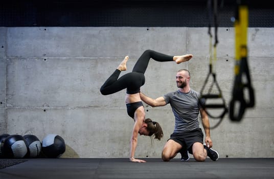 A muscular man assisting a fit woman in a modern gym as they engage in various body exercises and muscle stretches, showcasing their dedication to fitness and benefiting from teamwork and support.