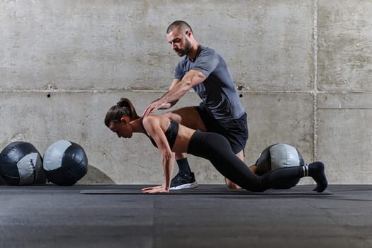 A muscular man assisting a fit woman in a modern gym as they engage in various body exercises and muscle stretches, showcasing their dedication to fitness and benefiting from teamwork and support.