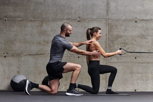 A muscular man assisting a fit woman in a modern gym as they engage in various body exercises and muscle stretches, showcasing their dedication to fitness and benefiting from teamwork and support.