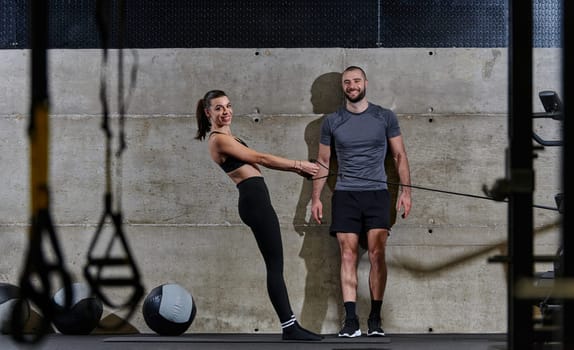 A muscular man assisting a fit woman in a modern gym as they engage in various body exercises and muscle stretches, showcasing their dedication to fitness and benefiting from teamwork and support.