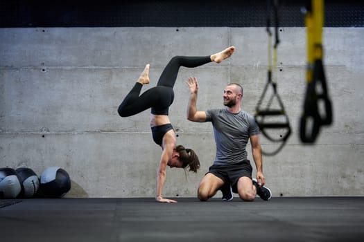 A muscular man assisting a fit woman in a modern gym as they engage in various body exercises and muscle stretches, showcasing their dedication to fitness and benefiting from teamwork and support.