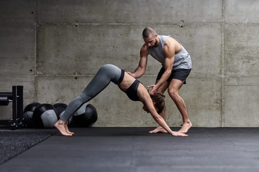 A muscular man assisting a fit woman in a modern gym as they engage in various body exercises and muscle stretches, showcasing their dedication to fitness and benefiting from teamwork and support.