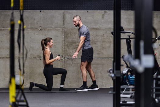 A muscular man assisting a fit woman in a modern gym as they engage in various body exercises and muscle stretches, showcasing their dedication to fitness and benefiting from teamwork and support.