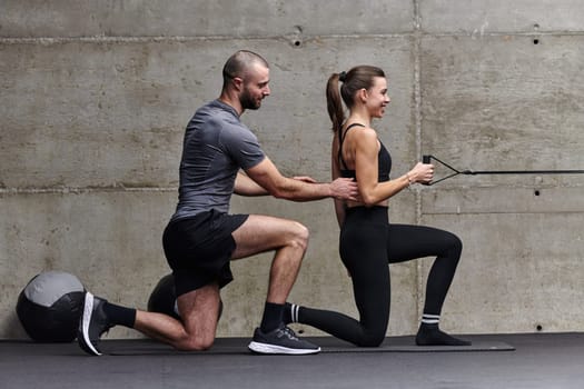 A muscular man assisting a fit woman in a modern gym as they engage in various body exercises and muscle stretches, showcasing their dedication to fitness and benefiting from teamwork and support.