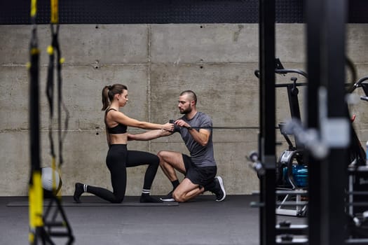 A muscular man assisting a fit woman in a modern gym as they engage in various body exercises and muscle stretches, showcasing their dedication to fitness and benefiting from teamwork and support.