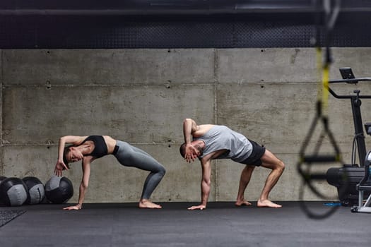 An attractive couple in the gym engaging in various stretching exercises together, showcasing their dedication to fitness, flexibility, and overall wellbeing. With synchronized movements, they demonstrate coordination, balance, and endurance while supporting and motivating each other on their fitness journey.