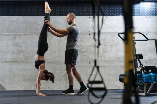 A muscular man assisting a fit woman in a modern gym as they engage in various body exercises and muscle stretches, showcasing their dedication to fitness and benefiting from teamwork and support.