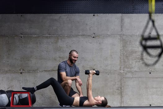 A muscular man assisting a fit woman in a modern gym as they engage in various body exercises and muscle stretches, showcasing their dedication to fitness and benefiting from teamwork and support.