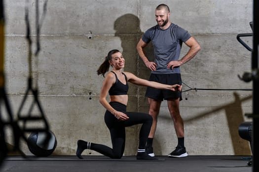 A muscular man assisting a fit woman in a modern gym as they engage in various body exercises and muscle stretches, showcasing their dedication to fitness and benefiting from teamwork and support.