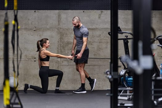 A muscular man assisting a fit woman in a modern gym as they engage in various body exercises and muscle stretches, showcasing their dedication to fitness and benefiting from teamwork and support.