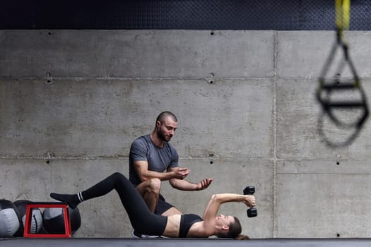 A muscular man assisting a fit woman in a modern gym as they engage in various body exercises and muscle stretches, showcasing their dedication to fitness and benefiting from teamwork and support.