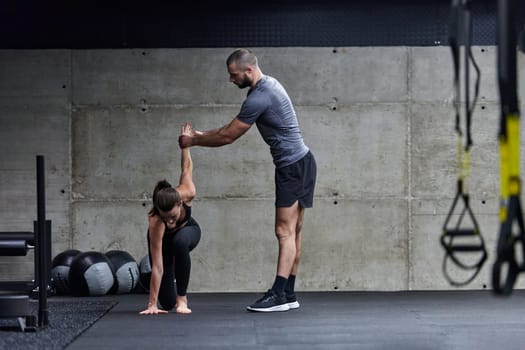 A muscular man assisting a fit woman in a modern gym as they engage in various body exercises and muscle stretches, showcasing their dedication to fitness and benefiting from teamwork and support.