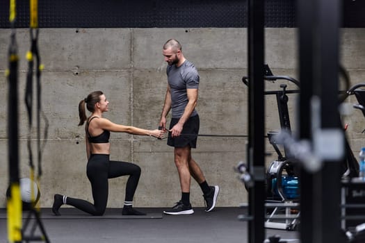 A muscular man assisting a fit woman in a modern gym as they engage in various body exercises and muscle stretches, showcasing their dedication to fitness and benefiting from teamwork and support.