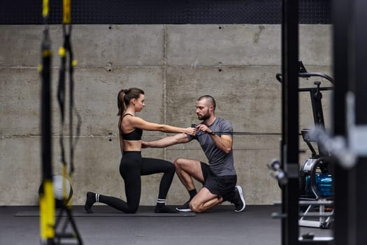 A muscular man assisting a fit woman in a modern gym as they engage in various body exercises and muscle stretches, showcasing their dedication to fitness and benefiting from teamwork and support.