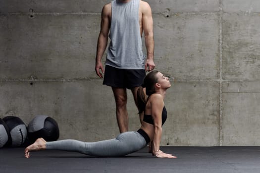 A muscular man assisting a fit woman in a modern gym as they engage in various body exercises and muscle stretches, showcasing their dedication to fitness and benefiting from teamwork and support.