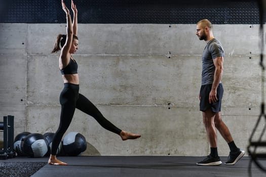 A muscular man assisting a fit woman in a modern gym as they engage in various body exercises and muscle stretches, showcasing their dedication to fitness and benefiting from teamwork and support.