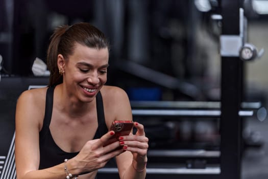 A fit woman in the gym taking a break from her training and uses her smartphone, embracing the convenience of technology to stay connected.