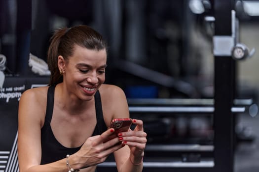 A fit woman in the gym taking a break from her training and uses her smartphone, embracing the convenience of technology to stay connected.