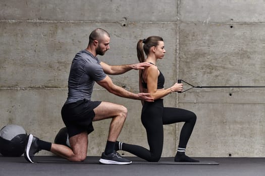 A muscular man assisting a fit woman in a modern gym as they engage in various body exercises and muscle stretches, showcasing their dedication to fitness and benefiting from teamwork and support.