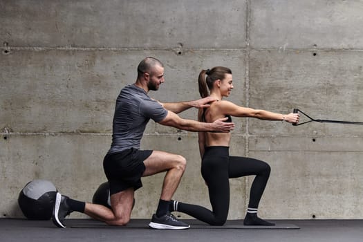 A muscular man assisting a fit woman in a modern gym as they engage in various body exercises and muscle stretches, showcasing their dedication to fitness and benefiting from teamwork and support.