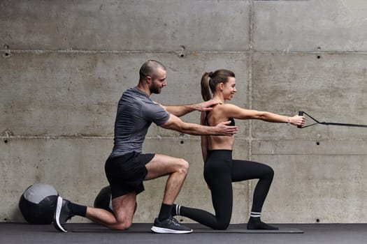 A muscular man assisting a fit woman in a modern gym as they engage in various body exercises and muscle stretches, showcasing their dedication to fitness and benefiting from teamwork and support.