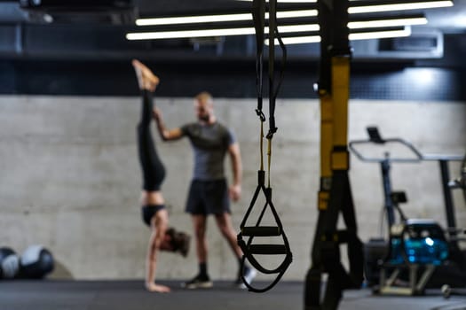 A muscular man assisting a fit woman in a modern gym as they engage in various body exercises and muscle stretches, showcasing their dedication to fitness and benefiting from teamwork and support.