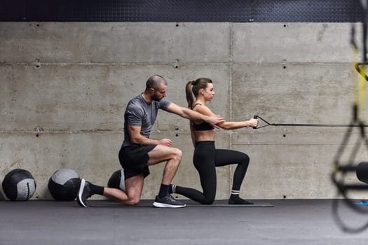 A muscular man assisting a fit woman in a modern gym as they engage in various body exercises and muscle stretches, showcasing their dedication to fitness and benefiting from teamwork and support.