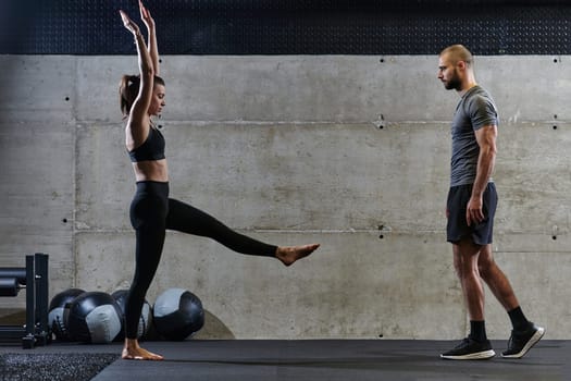 A muscular man assisting a fit woman in a modern gym as they engage in various body exercises and muscle stretches, showcasing their dedication to fitness and benefiting from teamwork and support.