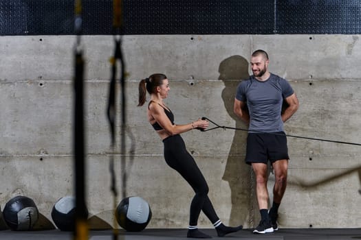 A muscular man assisting a fit woman in a modern gym as they engage in various body exercises and muscle stretches, showcasing their dedication to fitness and benefiting from teamwork and support.