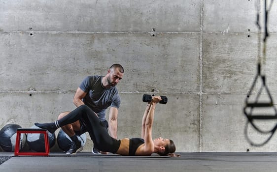 A muscular man assisting a fit woman in a modern gym as they engage in various body exercises and muscle stretches, showcasing their dedication to fitness and benefiting from teamwork and support.