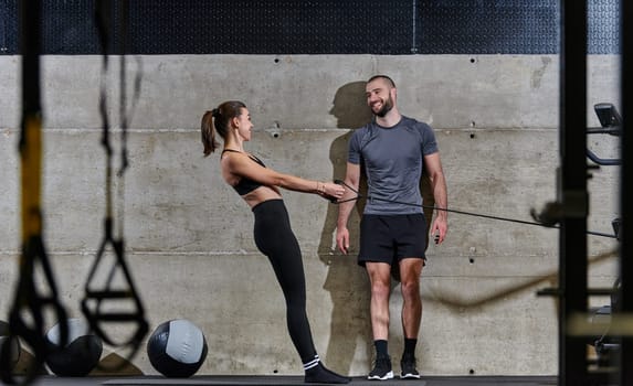 A muscular man assisting a fit woman in a modern gym as they engage in various body exercises and muscle stretches, showcasing their dedication to fitness and benefiting from teamwork and support.