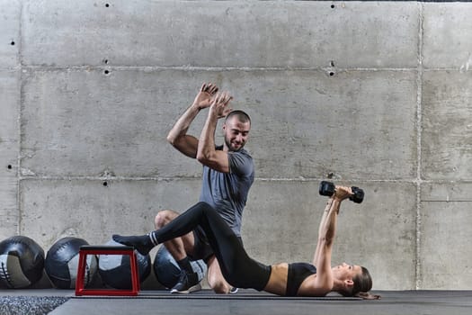 A muscular man assisting a fit woman in a modern gym as they engage in various body exercises and muscle stretches, showcasing their dedication to fitness and benefiting from teamwork and support.