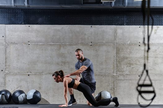 A muscular man assisting a fit woman in a modern gym as they engage in various body exercises and muscle stretches, showcasing their dedication to fitness and benefiting from teamwork and support.