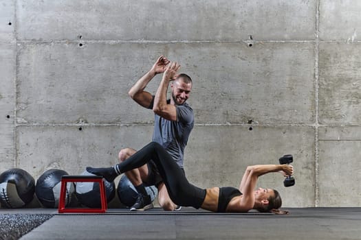 A muscular man assisting a fit woman in a modern gym as they engage in various body exercises and muscle stretches, showcasing their dedication to fitness and benefiting from teamwork and support.