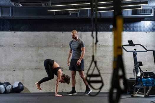 A muscular man assisting a fit woman in a modern gym as they engage in various body exercises and muscle stretches, showcasing their dedication to fitness and benefiting from teamwork and support.