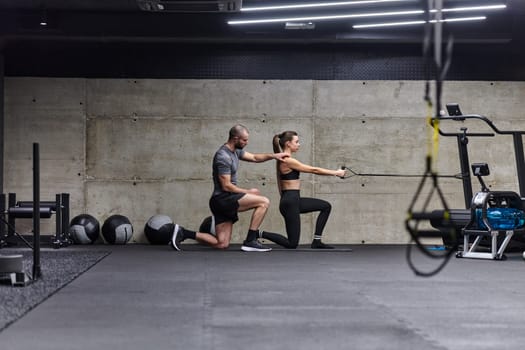 A muscular man assisting a fit woman in a modern gym as they engage in various body exercises and muscle stretches, showcasing their dedication to fitness and benefiting from teamwork and support.