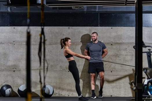 A muscular man assisting a fit woman in a modern gym as they engage in various body exercises and muscle stretches, showcasing their dedication to fitness and benefiting from teamwork and support.