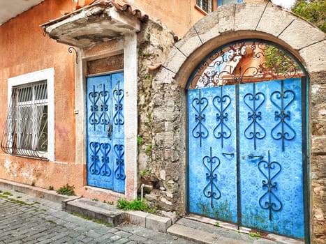 Facade of old village house with blue door and gate, with patterned forging