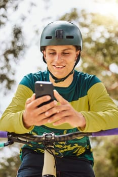 Mountain bike, phone and man outdoor in nature forest while online with a smile for communication or watching stunt video on internet. Athlete male with bicycle and smartphone for sports training.