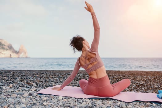 Middle aged well looking woman with black hair doing Pilates with the ring on the yoga mat near the sea on the pebble beach. Female fitness yoga concept. Healthy lifestyle, harmony and meditation.