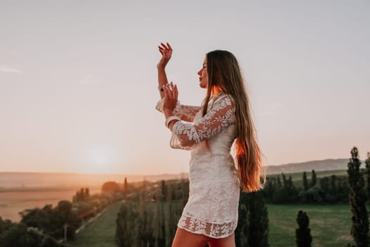 Romantic beautiful bride in white dress posing with sea and mountains in background. Stylish bride standing back on beautiful landscape of sea and mountains on sunset