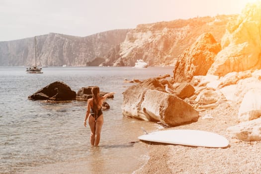 Woman travel sea. Young Happy woman in a long red dress posing on a beach near the sea on background of volcanic rocks, like in Iceland, sharing travel adventure journey