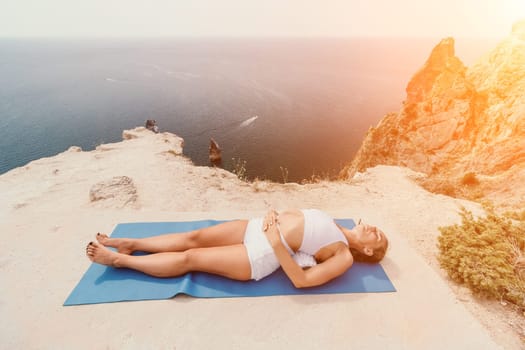 Middle aged well looking woman with black hair doing Pilates with the ring on the yoga mat near the sea on the pebble beach. Female fitness yoga concept. Healthy lifestyle, harmony and meditation.